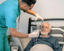 nurse helping older patient with oxygen mask at home