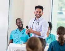 Young male physician speaking to room of healthcare providers