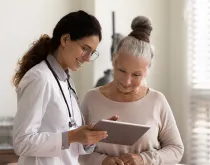 Happy doctor and senior patient use tablet at consultation 