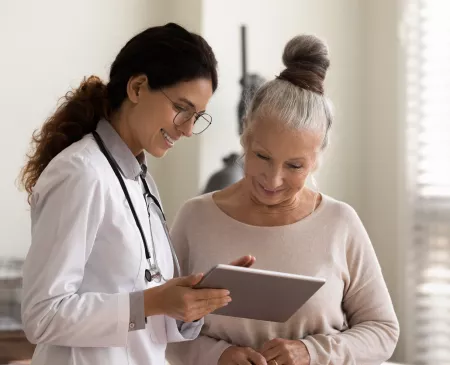 Happy doctor and senior patient use tablet at consultation 