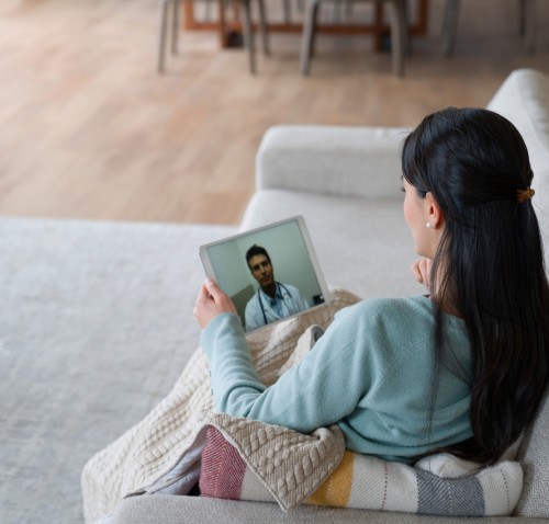 woman on couch having virtual appointment with doctor on tablet